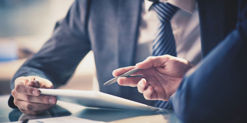 Image of two young businessmen using touchpad at meeting